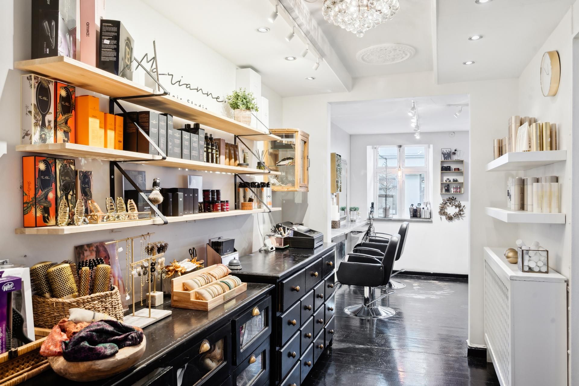 Butik med salonstole, hårplejeprodukter, og hylder med sort og lyseblå møbler i en hvid interiør