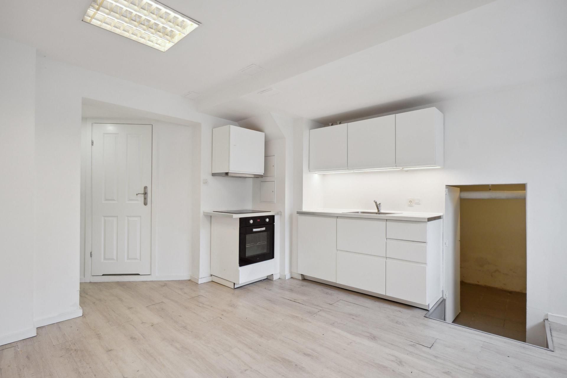 En nyrenoveret kælderlejlighed med moderne køkken og hvide vægge samt moderne gulv. Køkken med ovn og vask samt indbygget