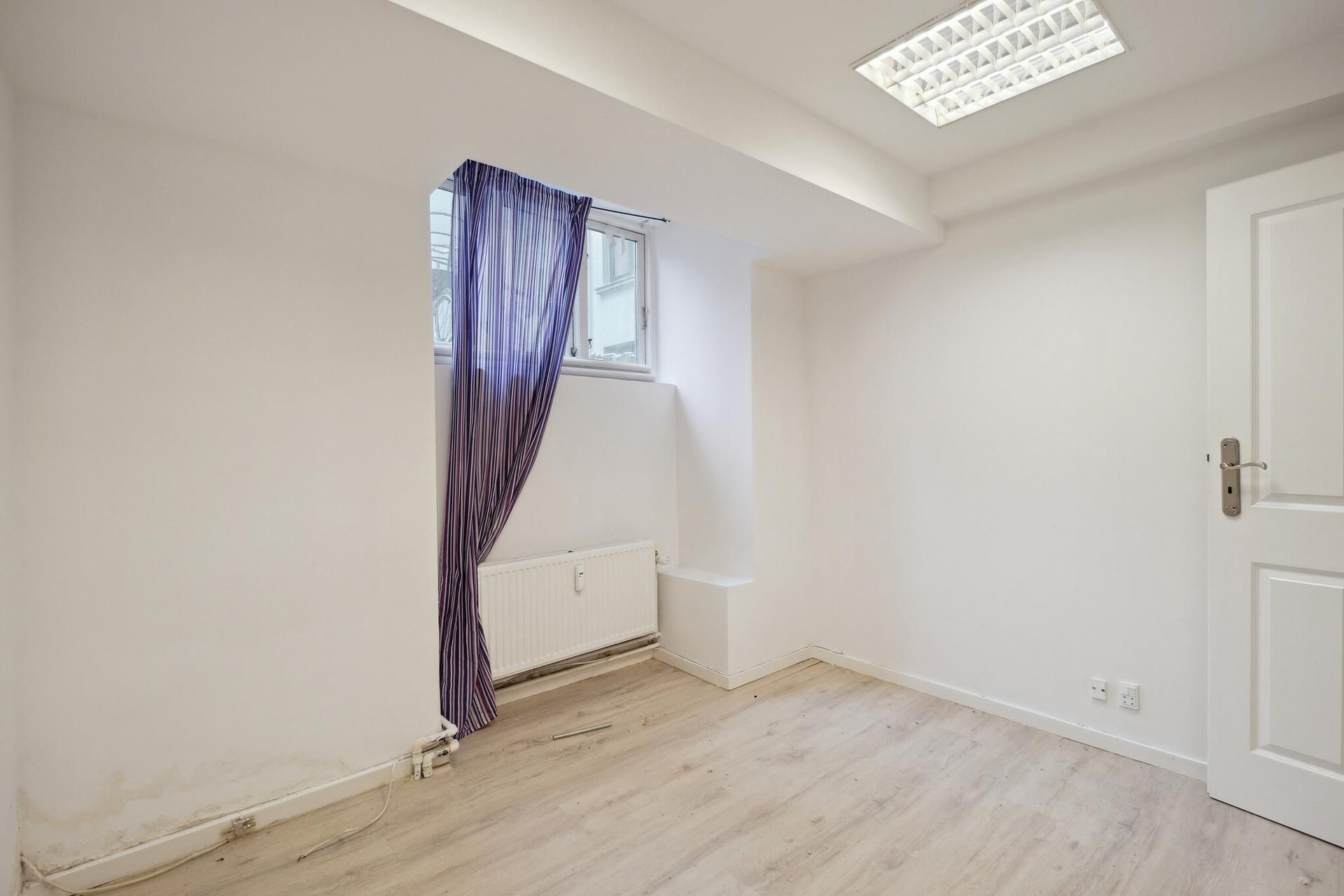 Indvendigt lejemål med hvide vægge og lyse trægulve, møbler og udstyr er til stede, såsom radiator, og en hvid dør