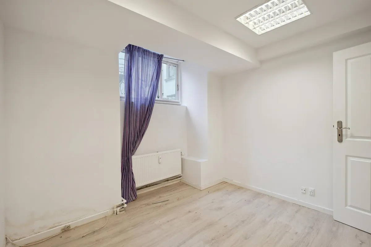 Indvendigt lejemål med hvide vægge og lyse trægulve, møbler og udstyr er til stede, såsom radiator, og en hvid dør