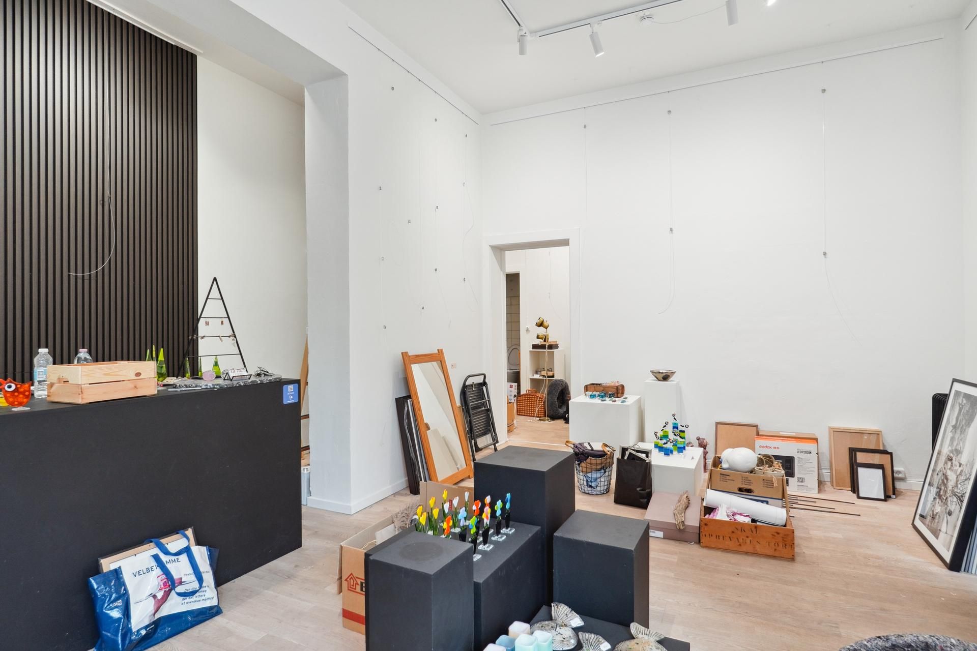 Butik med lyse loftsbøjler og udstillingsgenstande som et spejl, en lampe og flere kasser på gulvet