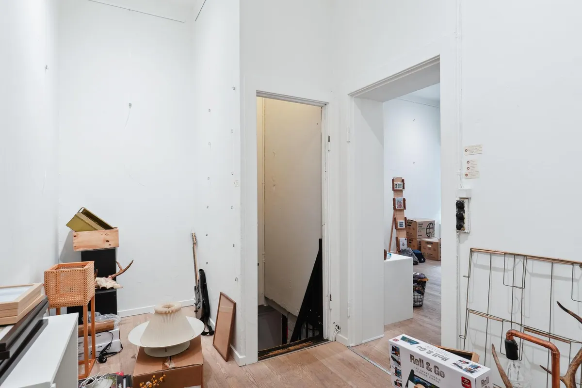 Foto af møbleret lejlighed med forskellige genstande og bokse samt et lukket trappekammer og 2 døre i baggrunden