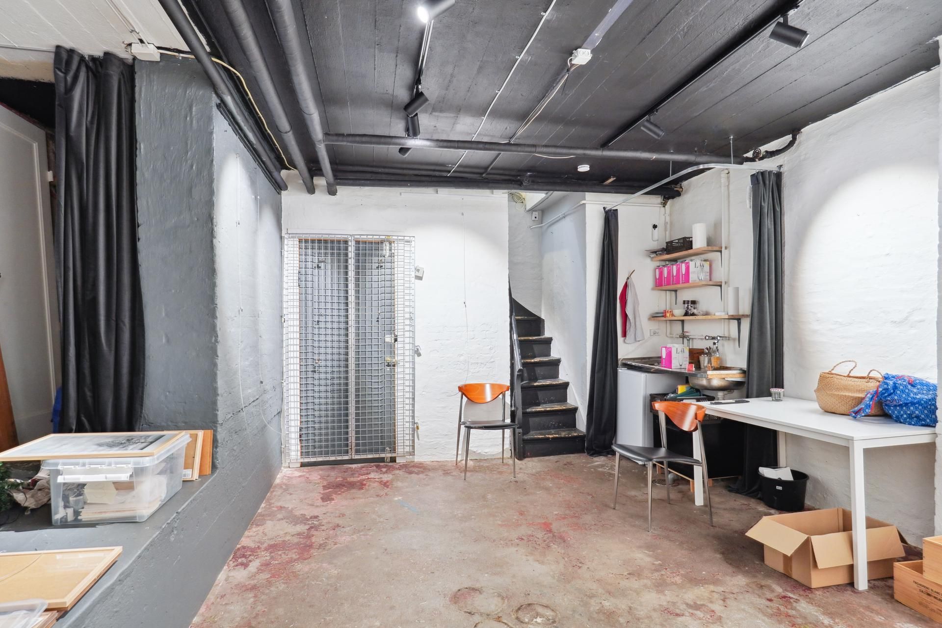 En loftslejlighed med to stolpe, højloft, stige, køkken, skrivebord, søjler og et skur op mod en væg med hængekurv og