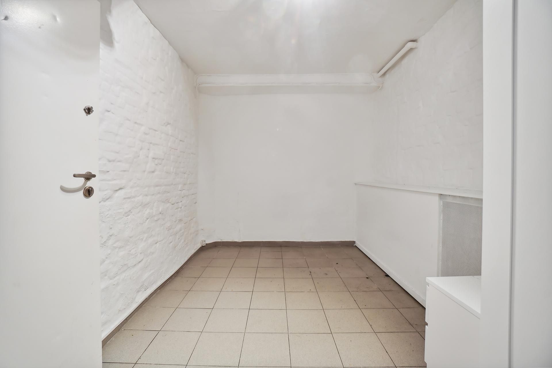 En stor, hvid og tom kælder med betongulve og hvide vægge og døre, der er åbne mod det indre rum