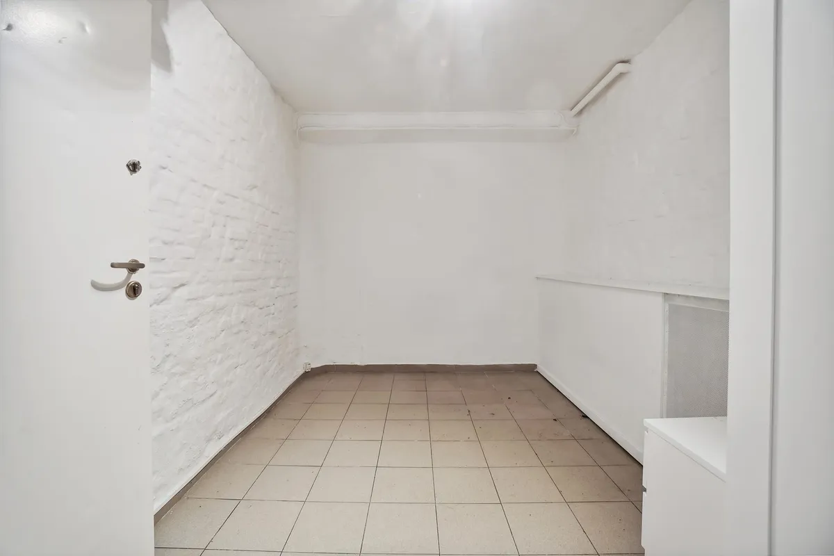 En stor, hvid og tom kælder med betongulve og hvide vægge og døre, der er åbne mod det indre rum