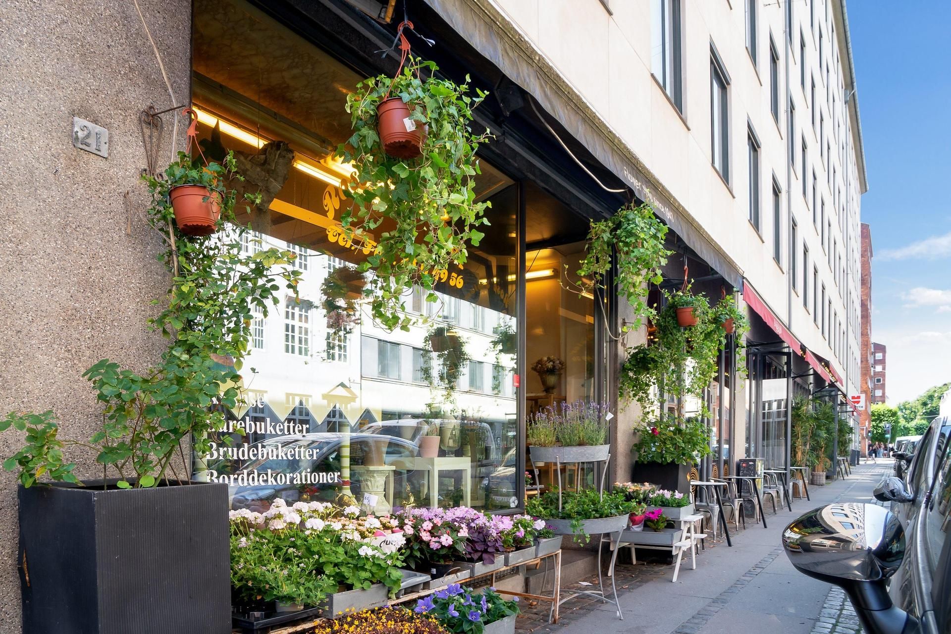 Butik med blomster på butiksvinduet og udendørs, træplanter og blomsterpotter, gulvet med blomster og en stol