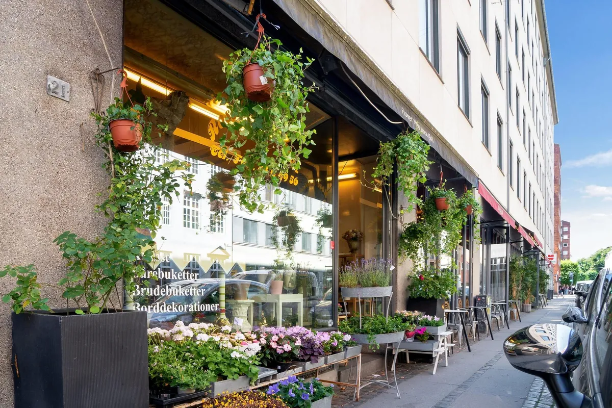 Butik med blomster på butiksvinduet og udendørs, træplanter og blomsterpotter, gulvet med blomster og en stol