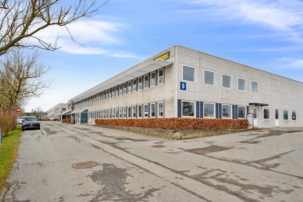 Et moderne kontorbygning med mærket Attodex på facaden, buske foran, og en bilparkeret i parkeringsplads.