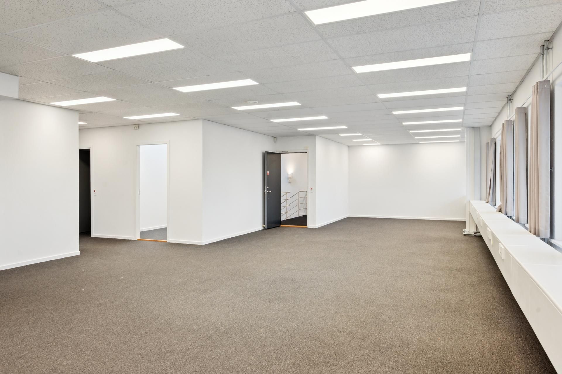 Rummelig og lys kontorlokal med lysegulv og hvide vægge. Lokaler med flere indgange, hvoraf én er åben. Værelserne er tømt