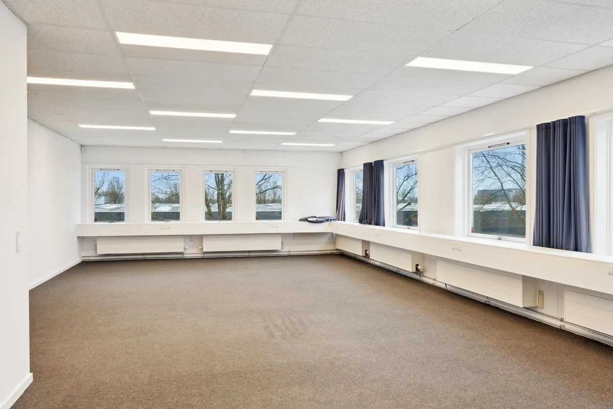 Kontorlokaler med store vinduer, hvide vægge og gulvbelægning samt smukke udsigt til skov og bjerge i baggrunden