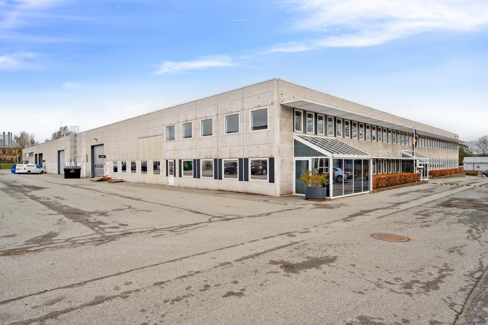 Kontorbygning med glasruder og garageindkørsler samt biler parkeret udenfor og plante i potte ved indgangen