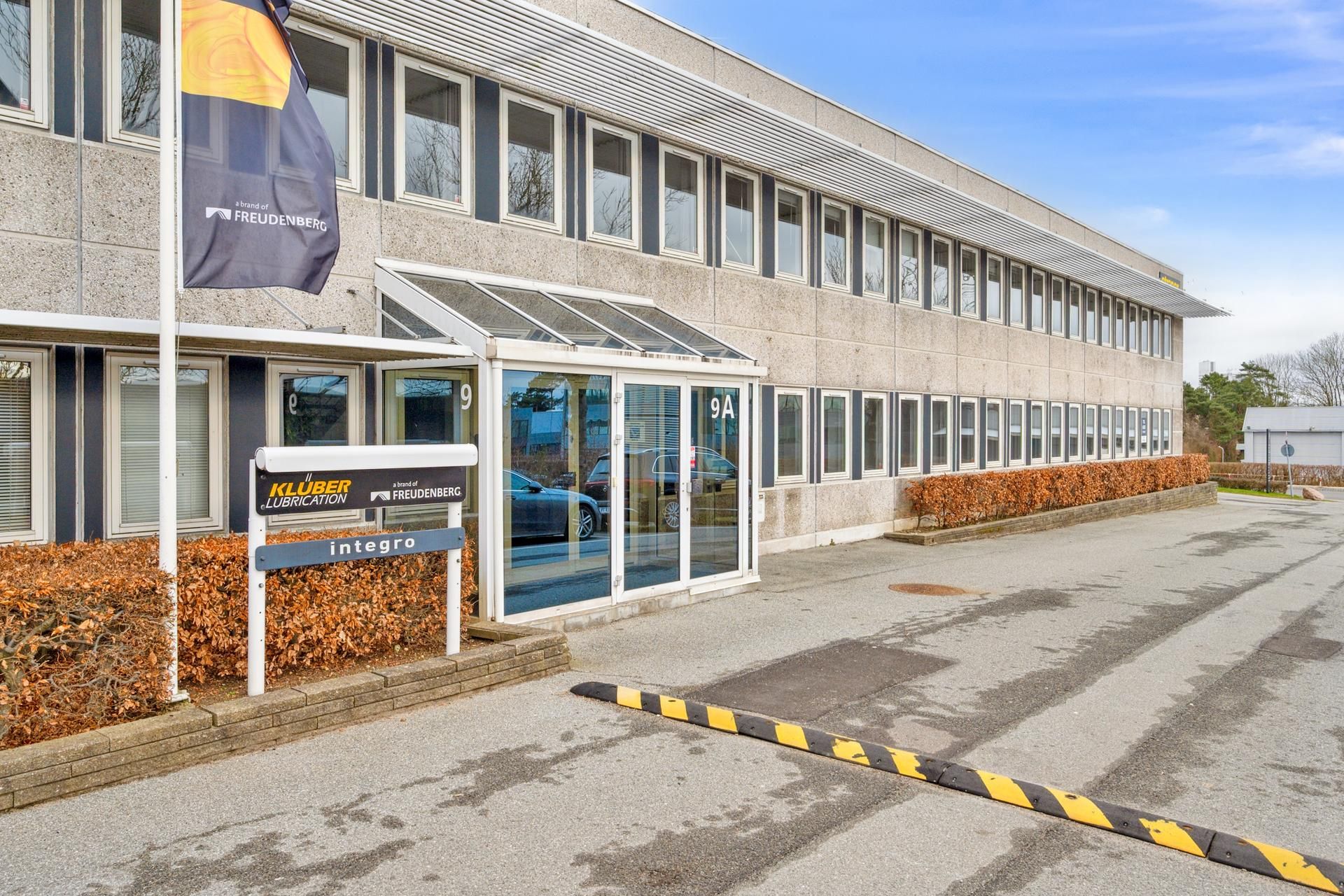Fronten af et kontorbygning med teksten Kluver Lubrication Integro og en flagpæl med et flag med teksten Freudenberg i