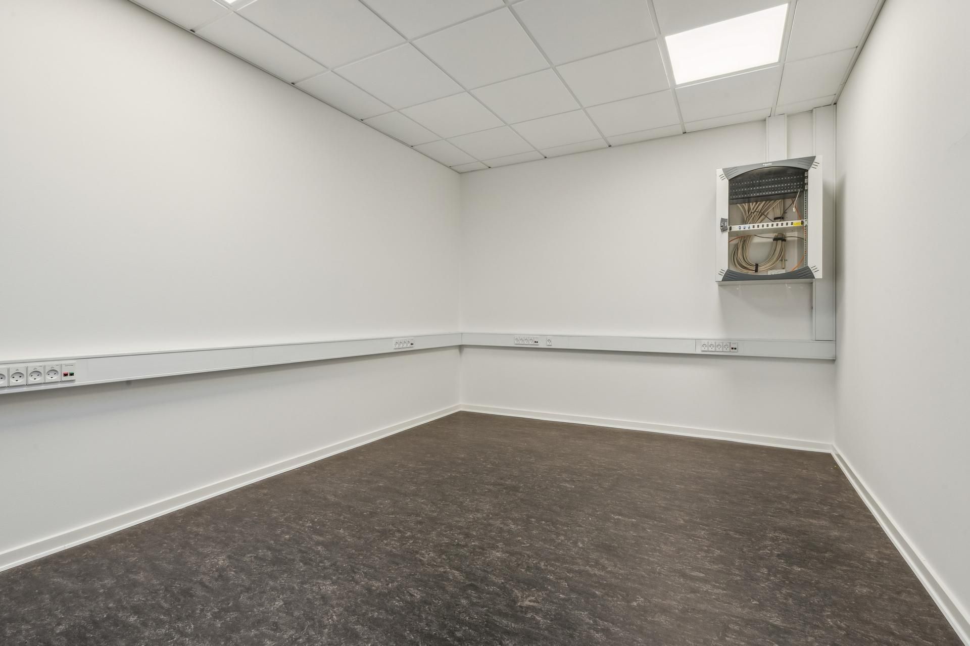 En tom kontorvæg med hvidt loft, hvor der er et stikkontaktpanel og en elektrisk skab med kabler på væggen