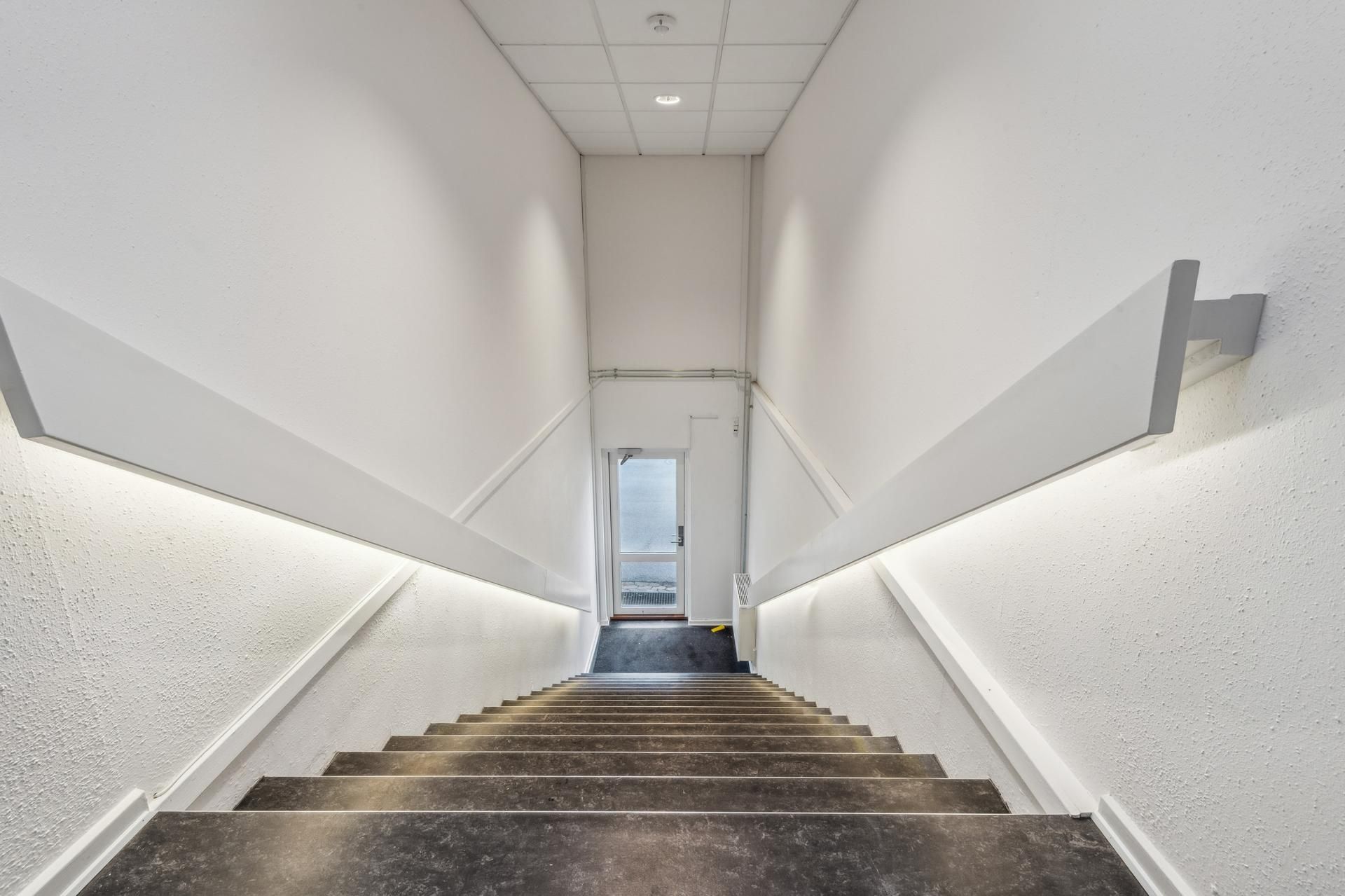 Moderne, minimalistisk trappe med hvide vægge og lys, der er installeret i højre sidevæg, gulv og loft