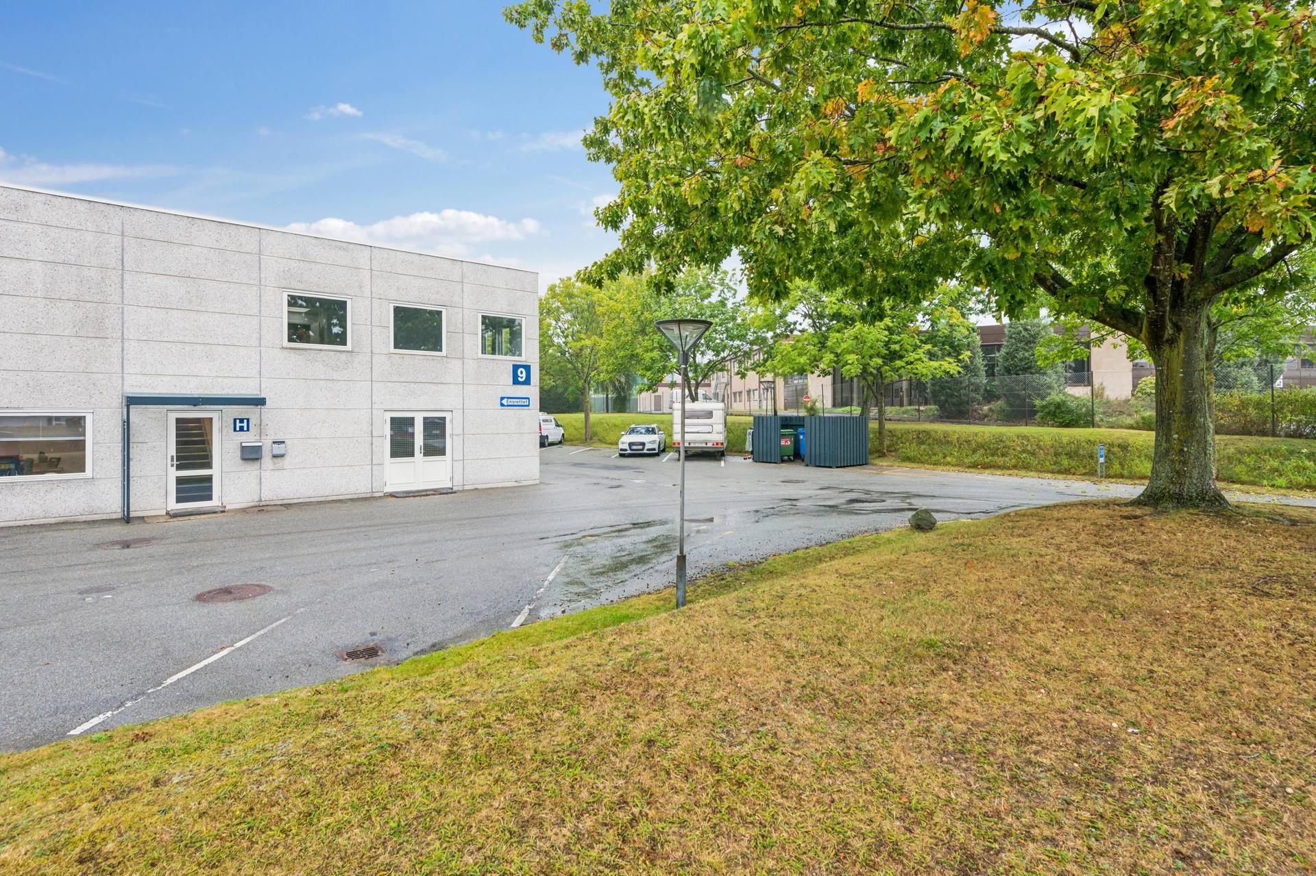 En stor, enkelt etage bygning med indgang, bilparkeringsplads, og træer og buske langs siderne