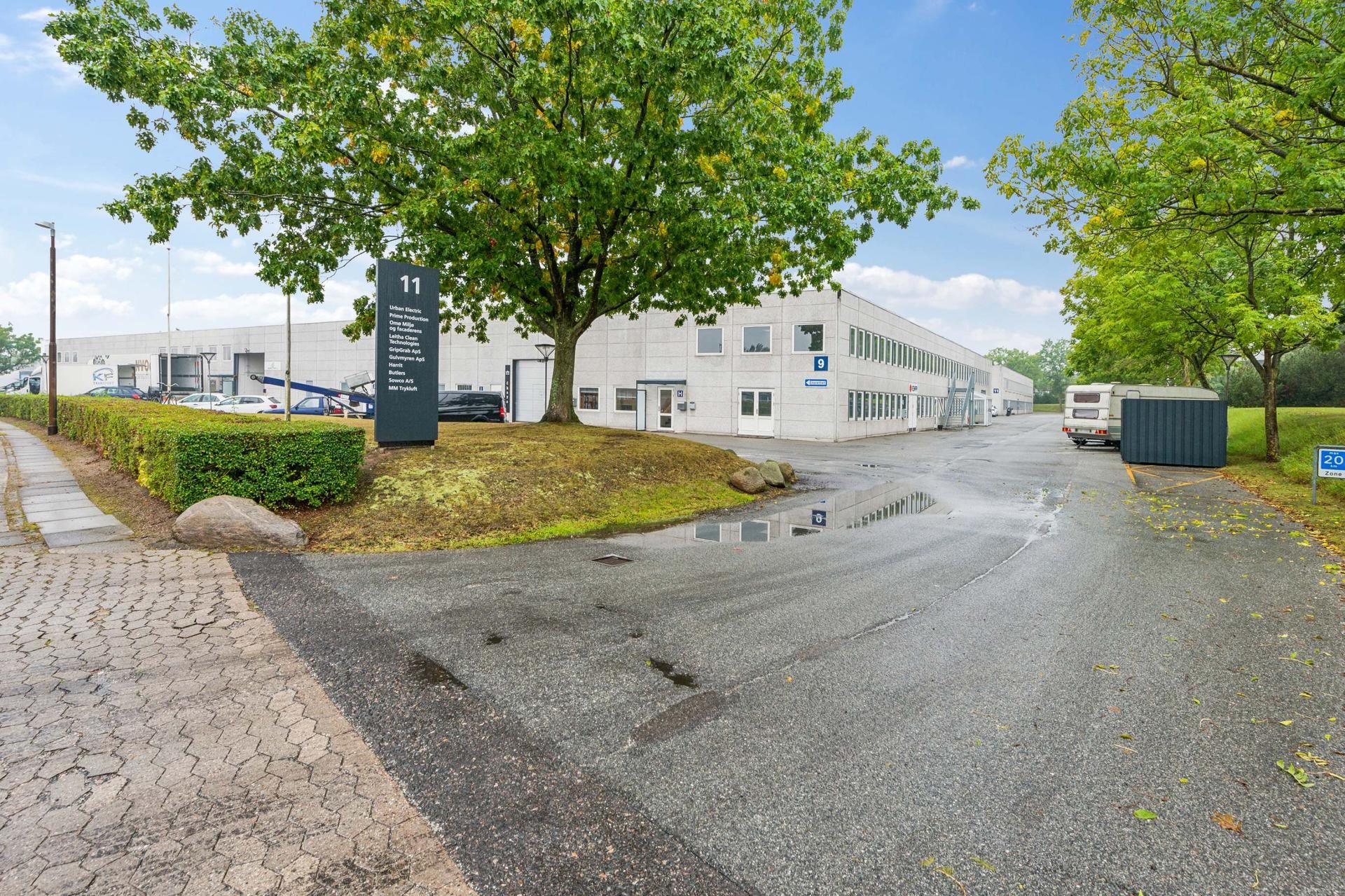 Kontorby i Køge med grønne områder, parkeringsplads og busstoppested foran bygningen