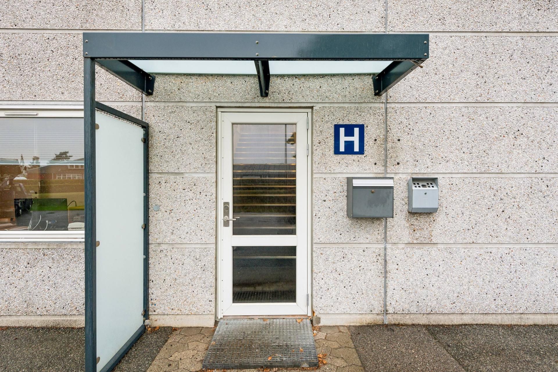 Glassdør og åben dør med en H i blå boks, postkasse og lysekroner i en bygning