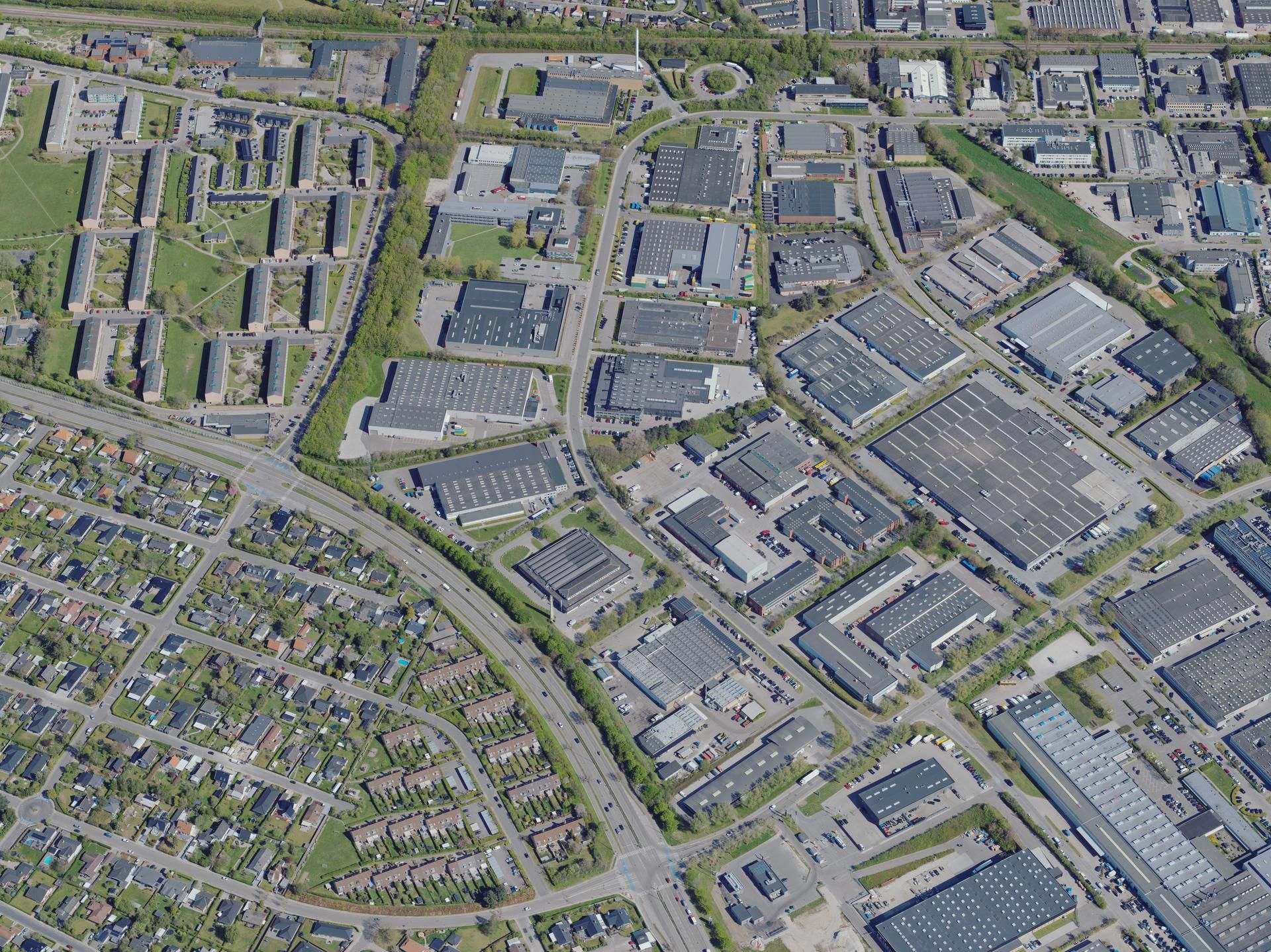 Billede af et forretningsdistrikt med en blanding af boliger og industribygninger. Der er veje og parkeringspladser, og