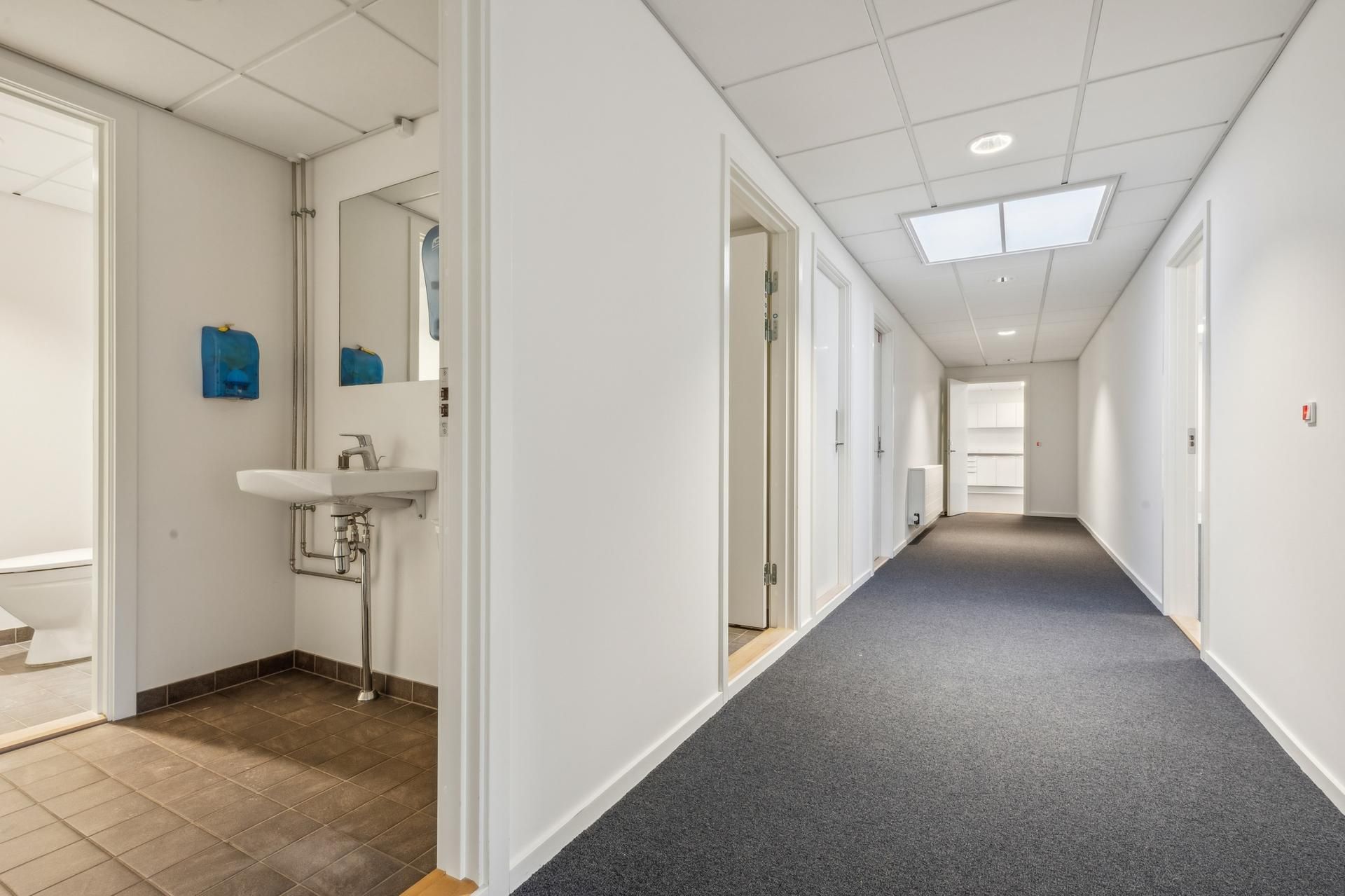 En lukket dør og en ren gang med lysegrå gulvtæppe og hvide vægge med lysekroner