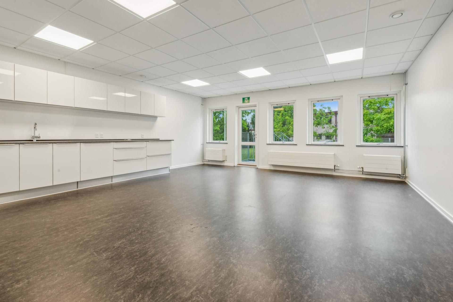 Kontor med hvide vægge, højloft, moderne kabiner og store ruder med udsigt til grønne træer