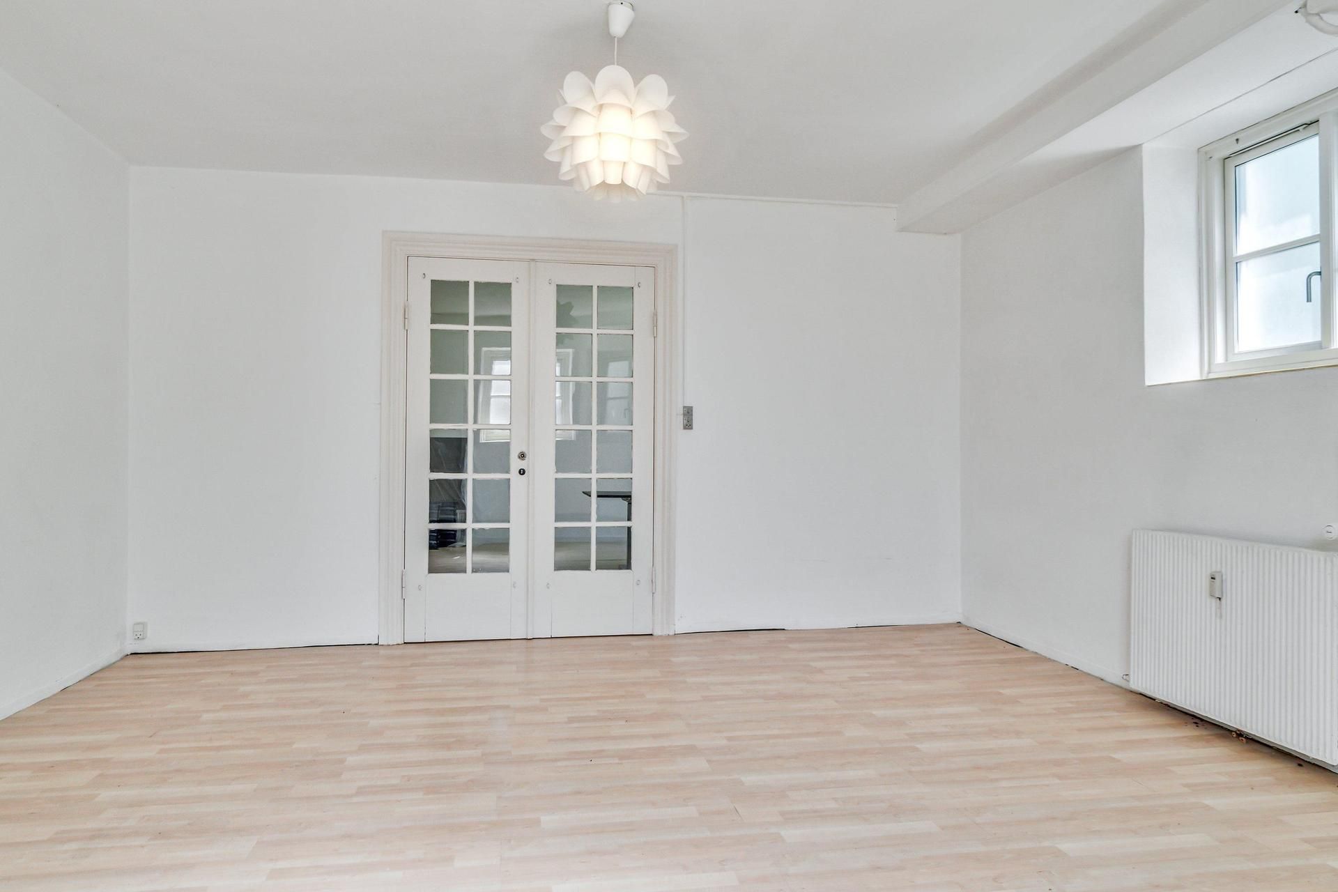 Et tomt rum med hvide vægge, et hvidt loft og en hvid dør med glasruder og en radiator