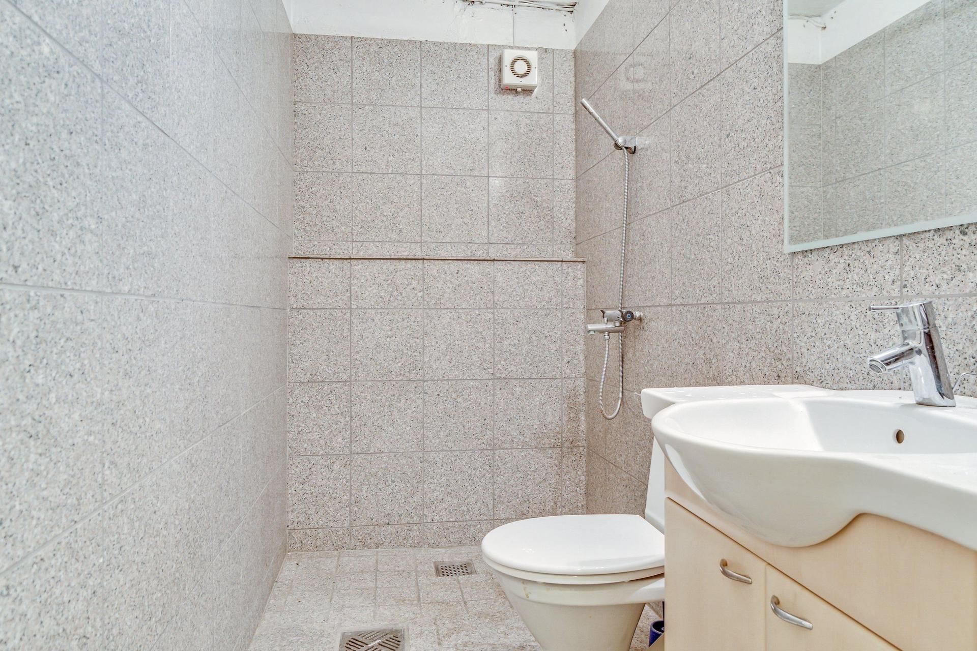 Et lille badeværelse med hvid tøjskab og spejl, toilet med hvidt sæde og håndklædestang samt en hvid vask med håndbruser