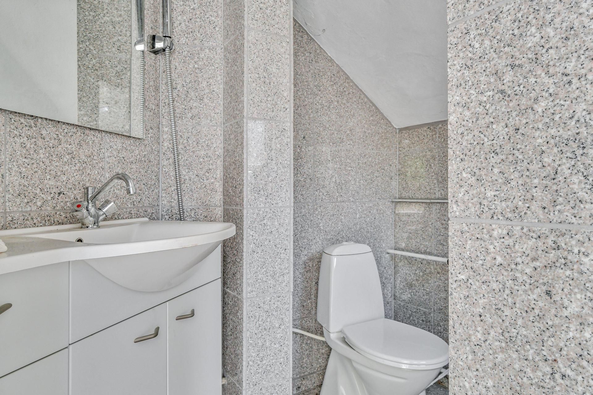 Badrum med hvidt toilet, hvid vask og spejl med stribet mønster samt håndtag og vandhane af sølv