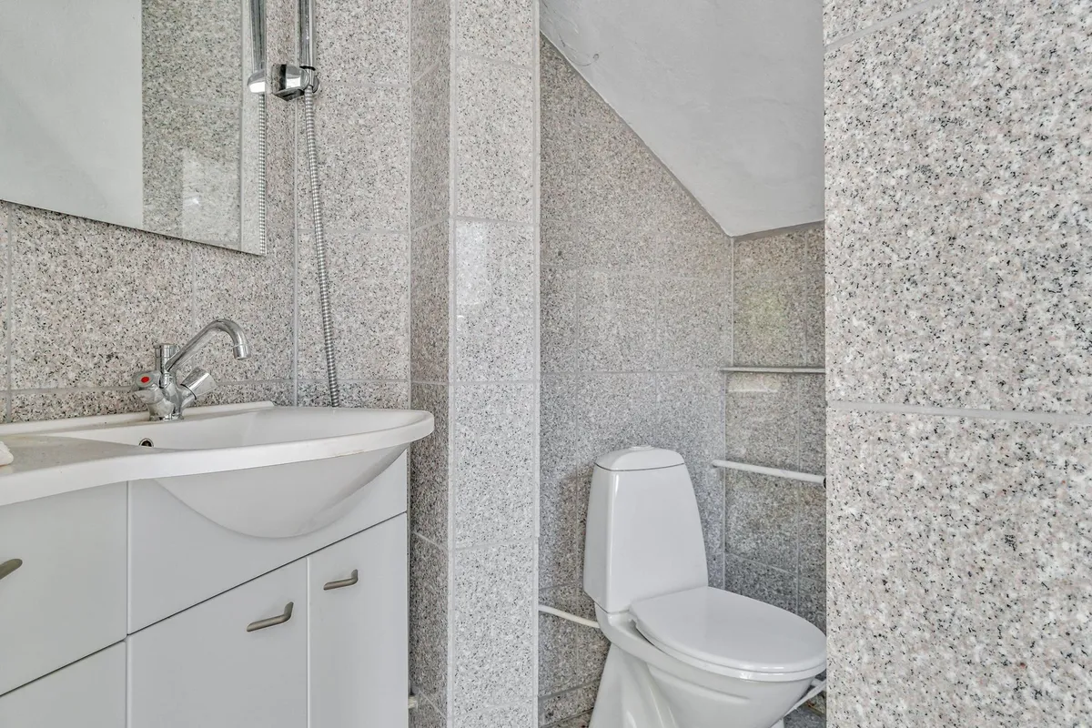 Badrum med hvidt toilet, hvid vask og spejl med stribet mønster samt håndtag og vandhane af sølv