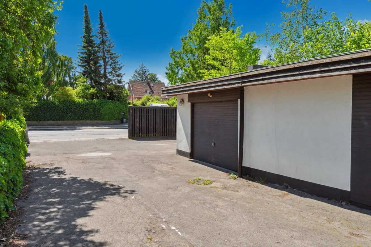 Garage med to parkeringspladser og indkørselsmulighed. Væggene er malet i hvidt og brunt. Der er et enkelt garagedør og en