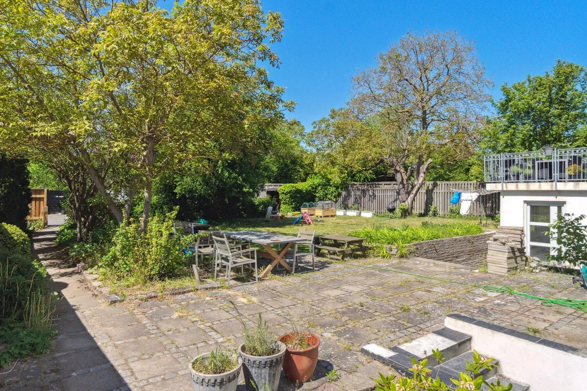 En smuk have med et stort træ, blomsterpotter, en træbord, bænke, en klatrevæg og et højt højhus