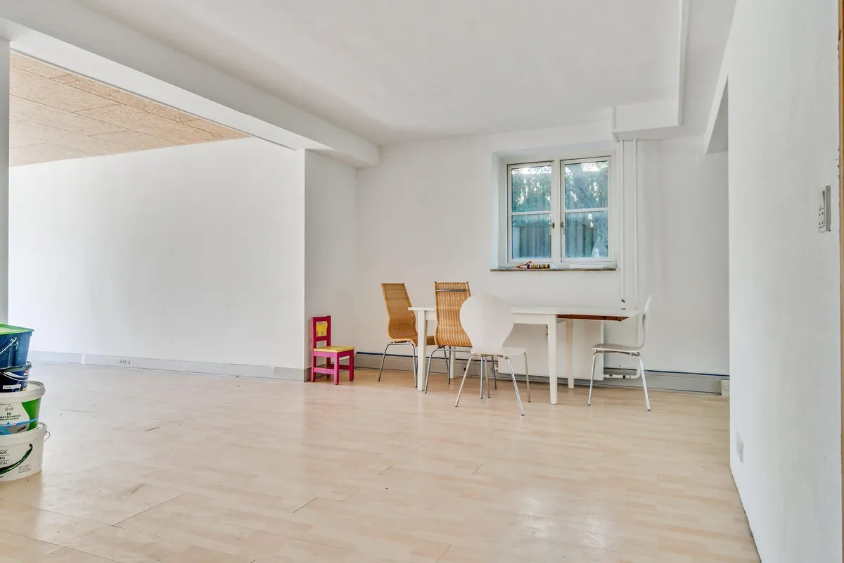 Hvidt lokale med trægulv og tre hvide stole samt en lille pink og hvid stol med skriftstykke på bordet