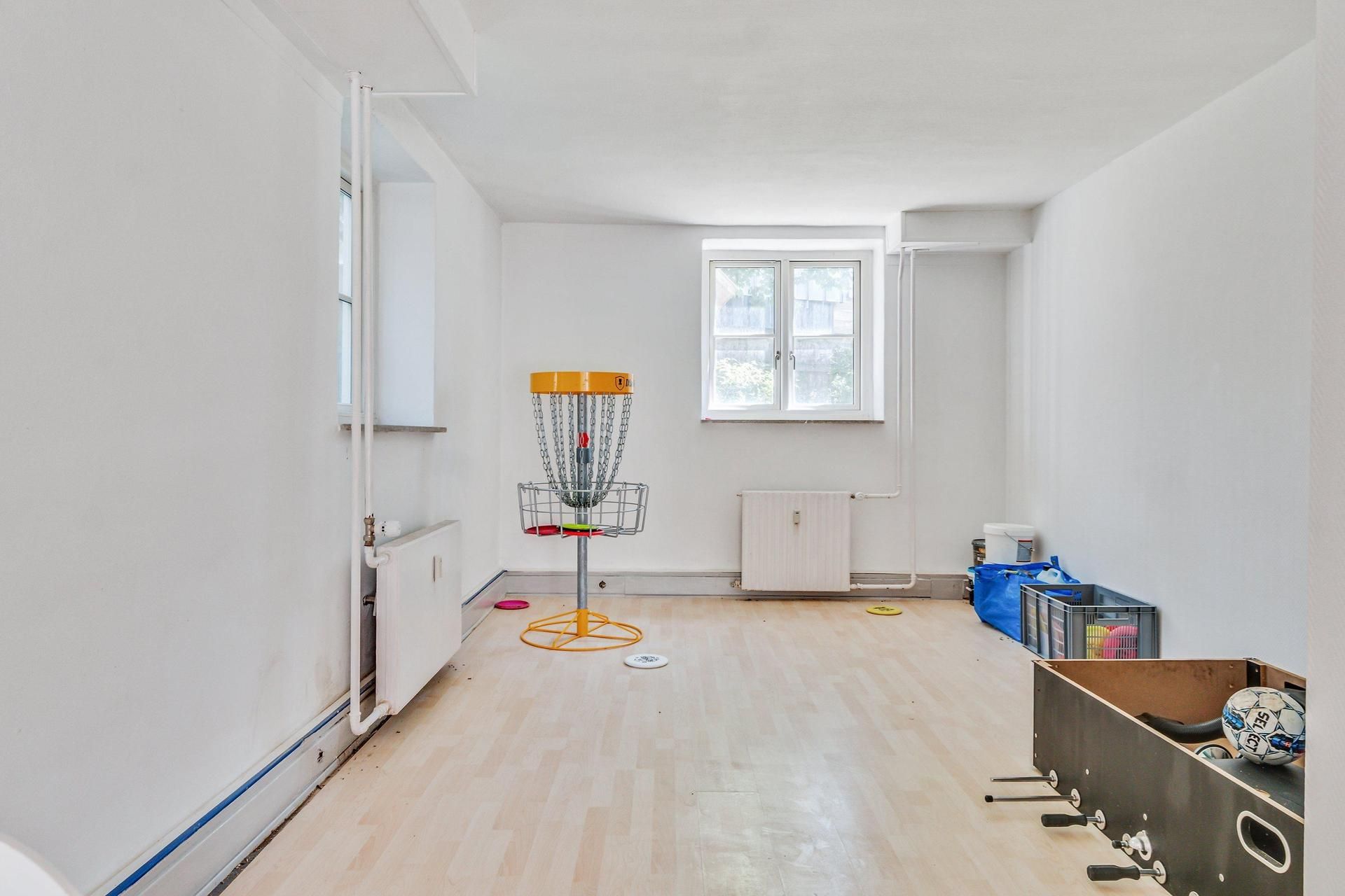En lys og ren kontorlokal med trægulv, frisbeegolfbane og et hvidt boldstativ, samt flere fritidslege og sportsudstyr