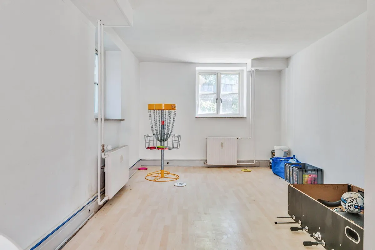 En lys og ren kontorlokal med trægulv, frisbeegolfbane og et hvidt boldstativ, samt flere fritidslege og sportsudstyr