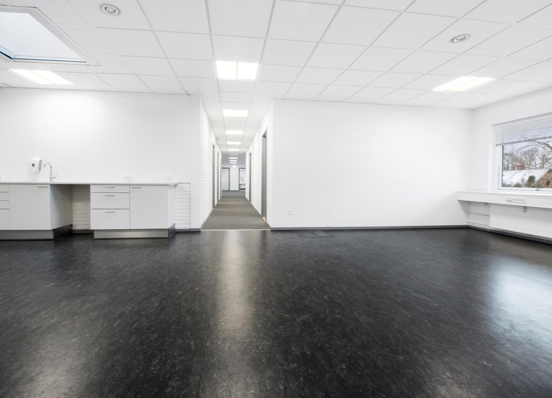 Et stort og lyst kontor med hvide vægge og gulv samt højt til loftet med hvide loftspaneler og indbygget lys