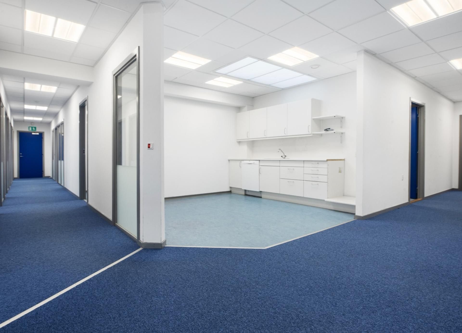 Indflytningsklare kontorlokaler med hvide vægge og lyse loftslamper, blå gulvbelægning og møbler samt en lysskur og et
