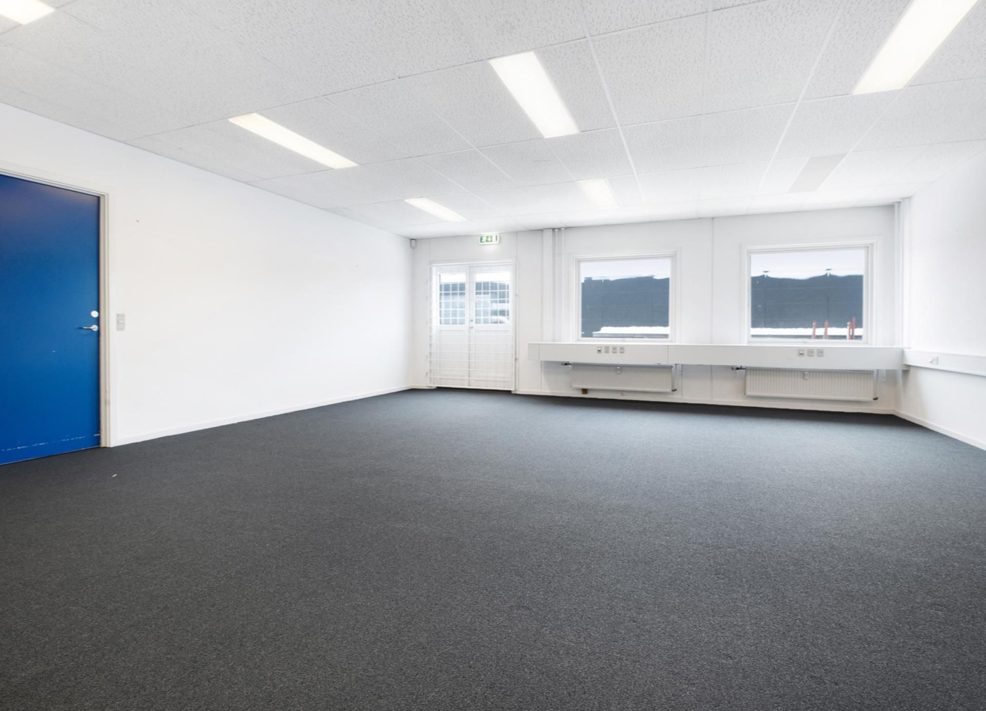 Ren og tom kontorlokal med hvide vægge og gulv samt to vinduer og et enkelt døre og møbler i hvidt