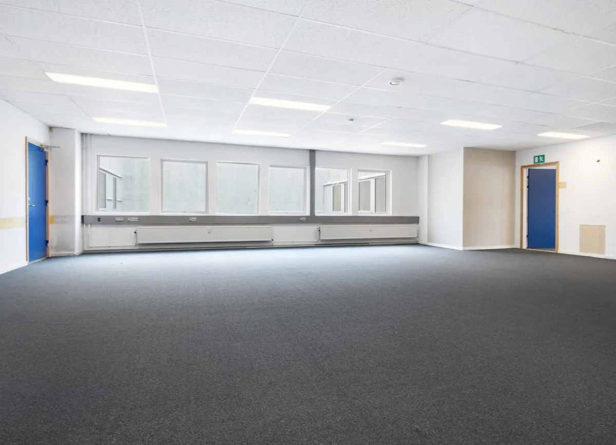 Store lokaler med hvide vægge og gulvbelægning, højt lyskabin og vinduer, to døre og radiatorer
