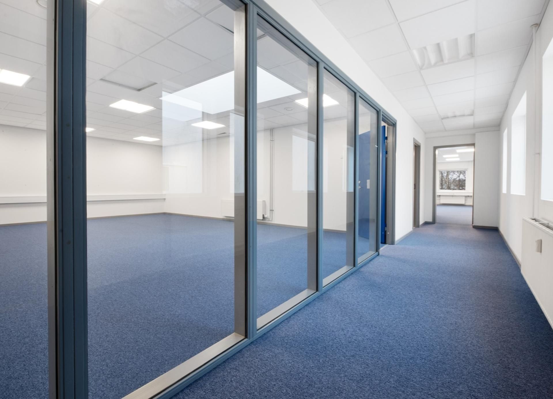 En tom og ren kontorrum med blå gulvbelægning og glasvinduer som reflekterer rummet