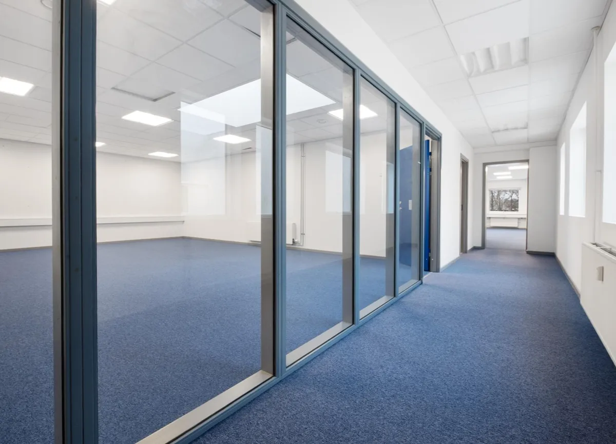 En tom og ren kontorrum med blå gulvbelægning og glasvinduer som reflekterer rummet