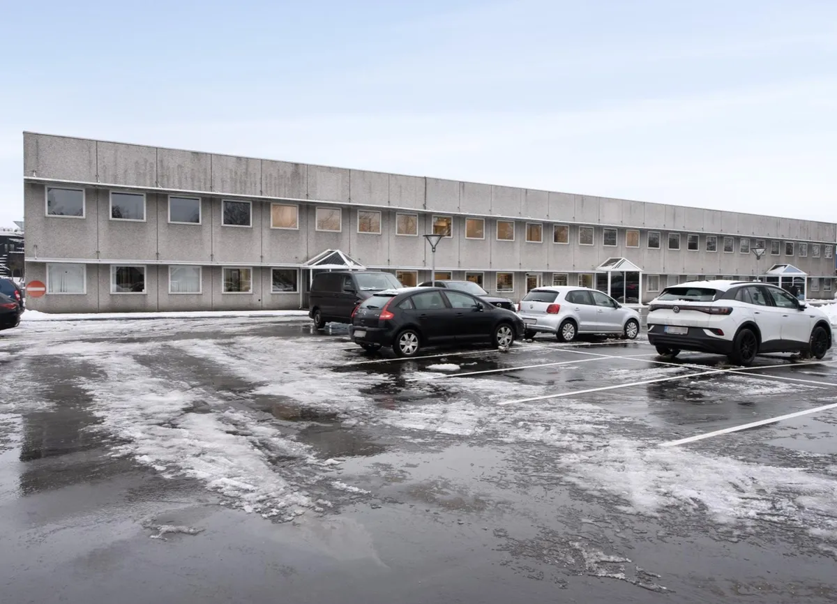Et stort kontorhuse med mange vinduer og en parkeringsplads med tre parkerede biler og meget sne