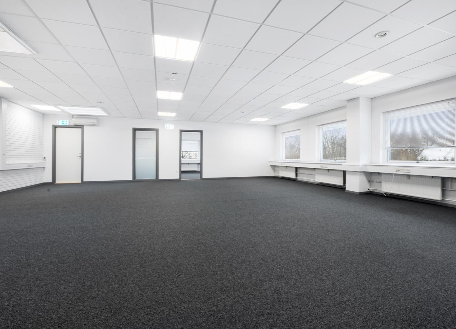 Et tomt kontor med hvide vægge, loftslampe og tre døre i enden af lokalet