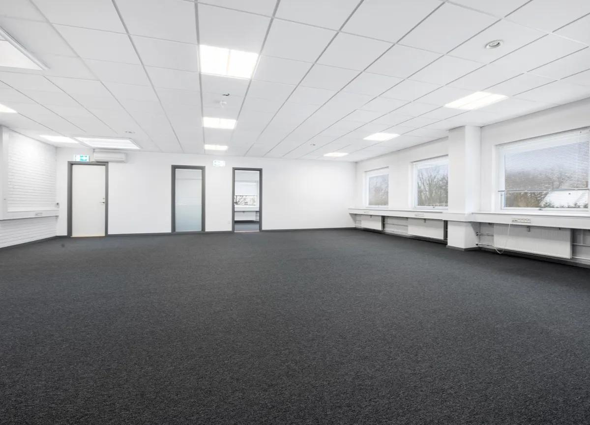 Et tomt kontor med hvide vægge, loftslampe og tre døre i enden af lokalet