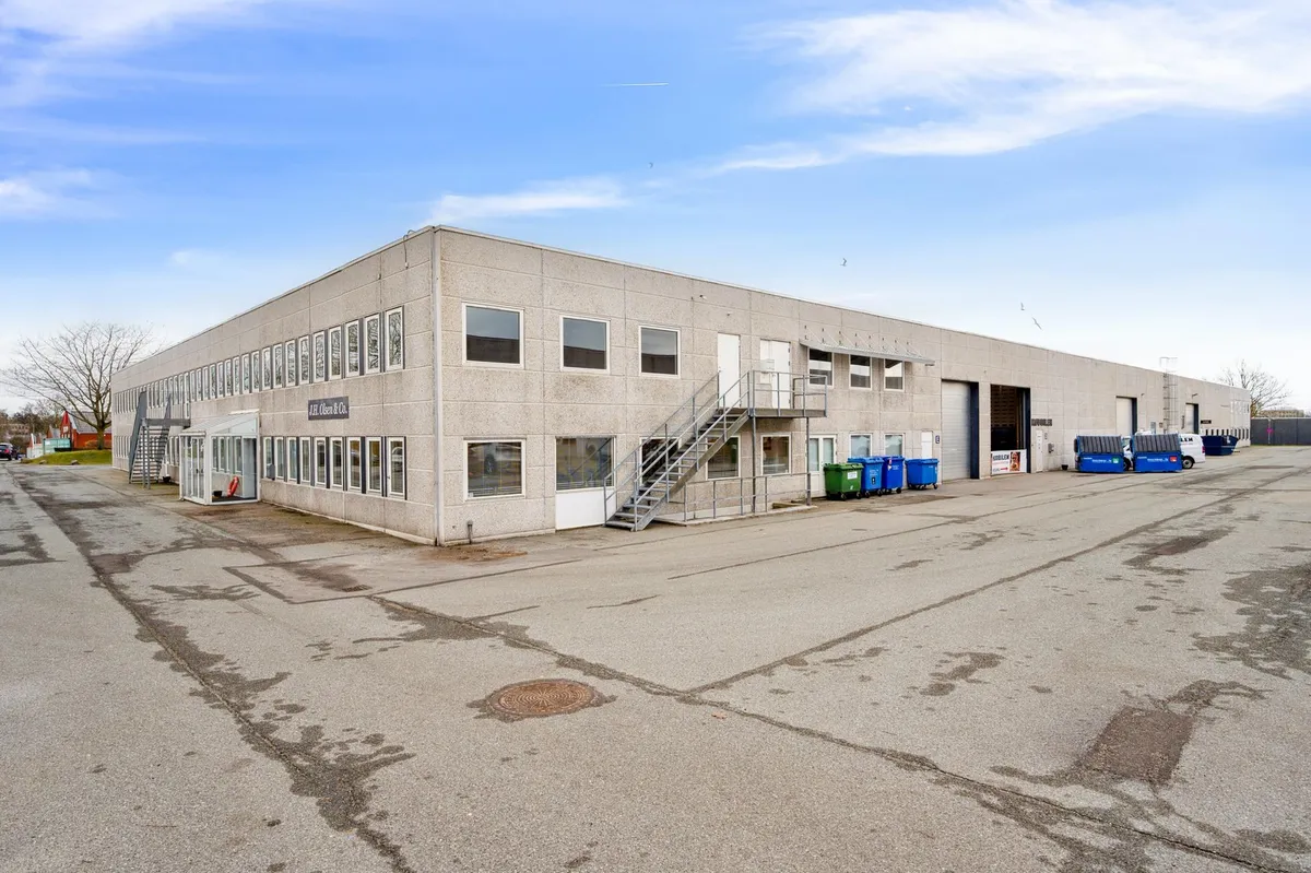 Kontorbyggeri med glasvinduer og opgang i Skovlunde. Foran bygningen er der et stort parkeringsområde med flere køretøjer og