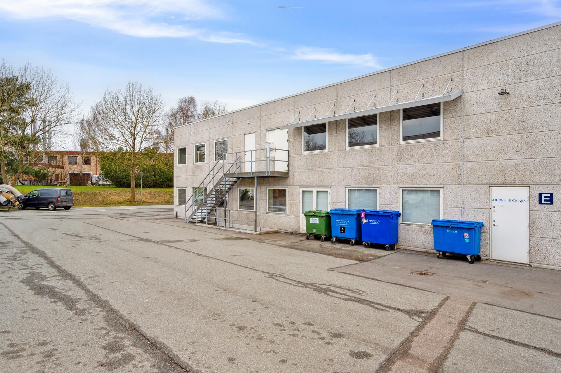 Kontorby i Skovlunde med flere farvede papirkurve, en trappe og to døre foran og bagved en bilparkeringsplads
