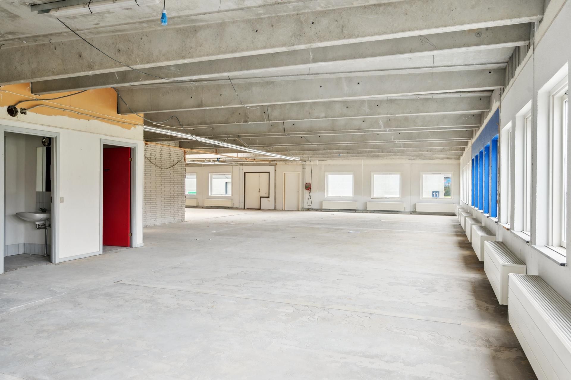 En tom og bred kontoret i Skovlunde med store vinduer, hvide vægge og gule loftsbjælker