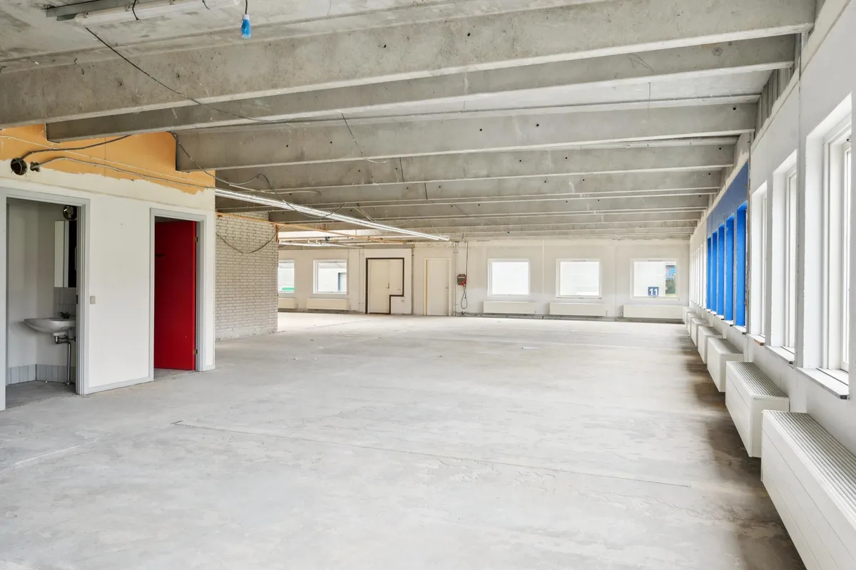 En tom og bred kontoret i Skovlunde med store vinduer, hvide vægge og gule loftsbjælker