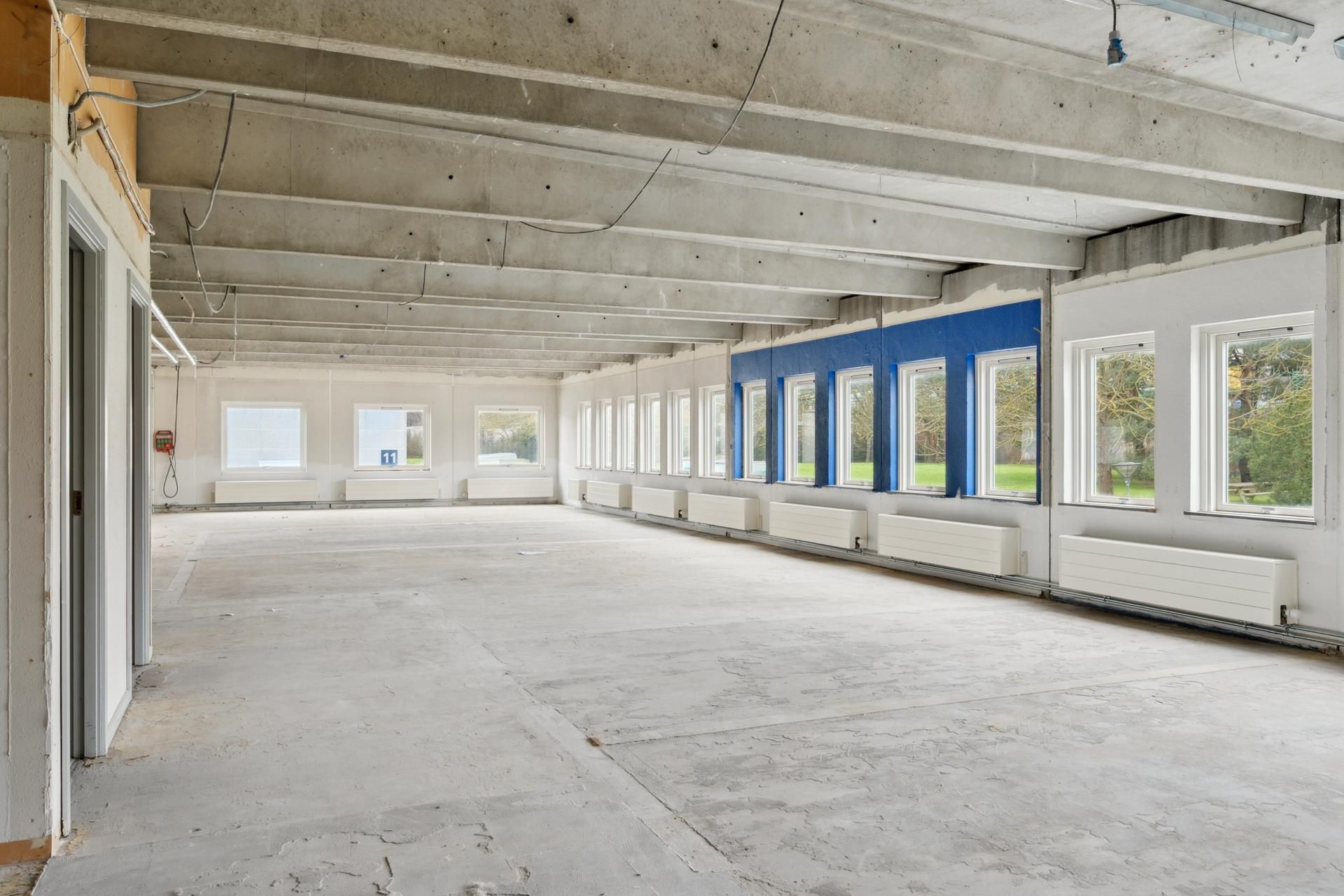 En stor kontorlokal med højt til loftet, vinduer og radiatorer langs væggen og en nummeret dør