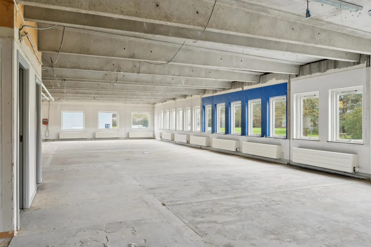 En stor kontorlokal med højt til loftet, vinduer og radiatorer langs væggen og en nummeret dør