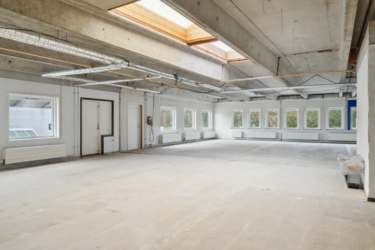 Store tomt kontorlokaler med højloft, lyskæder og hvide vægge, vinduer og døre samt åbne lofter og tekniske anlæg