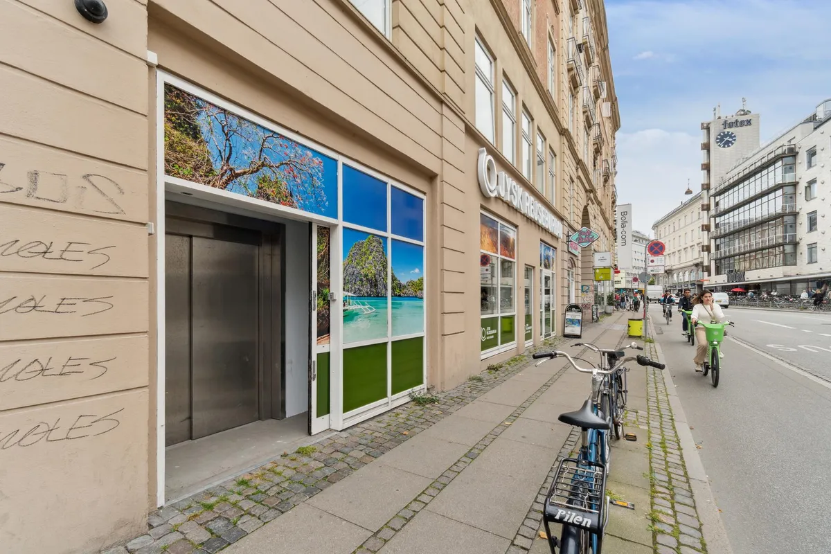 Bagefter graffiti på lagerbygning med skilte for Ouysx Reisebureau og flere cykler parkeret langs siden af en gågade på